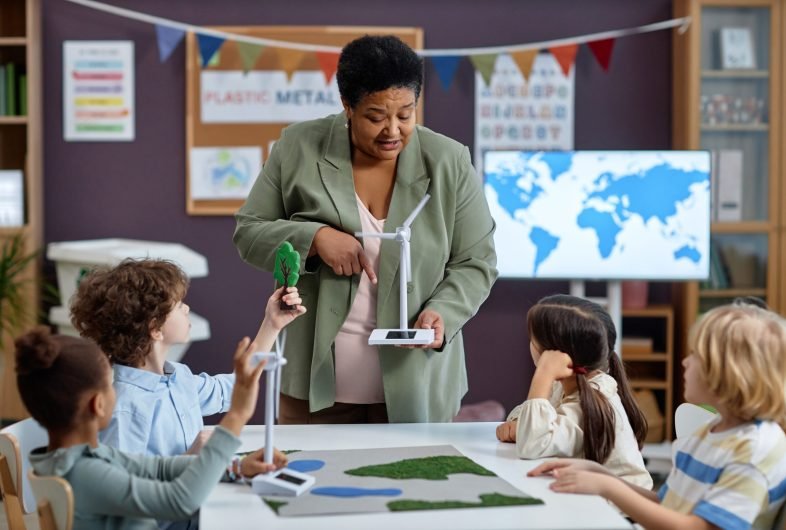 Waist up portrait of Black woman holding wind turbine model teaching group of children on clean energy in preschool