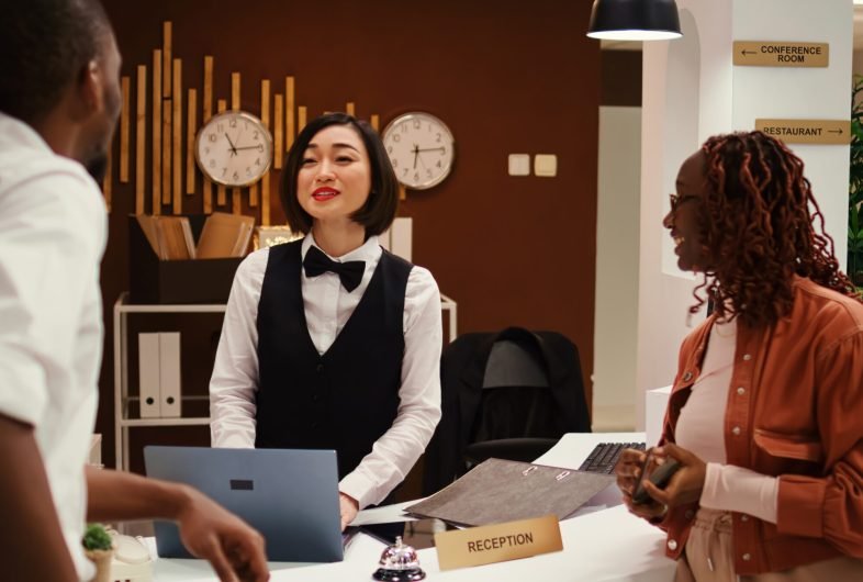 Friendly receptionist presenting holiday package options to african american couple in posh hotel. Husband and wife on honeymoon trip preparing to pay for extra room amenities in resort lounge