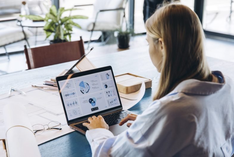 Businesswoman working on marketing strategy using charts displayed on laptop screen, developing innovative solutions for company growth in contemporary workspace. Online technology concept
